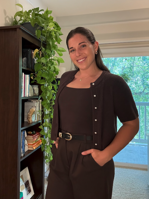 Amber, founder of Serenity Now Solutions, standing beside a bookshelf and a trailing pothos plant.