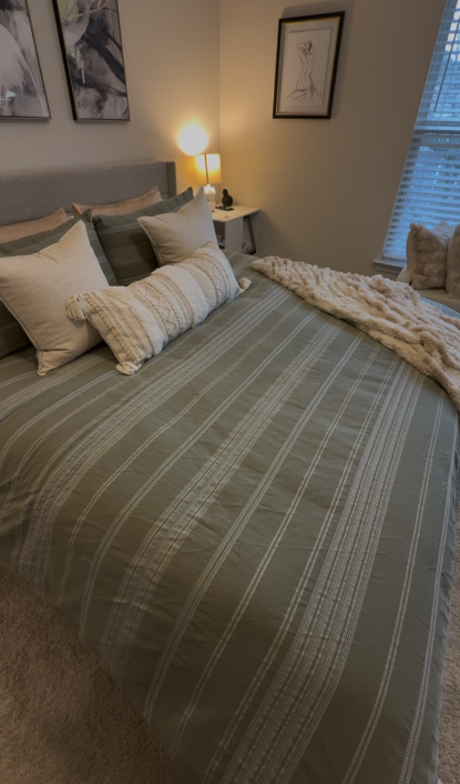 The same bedroom, bed made and surfaces clear.