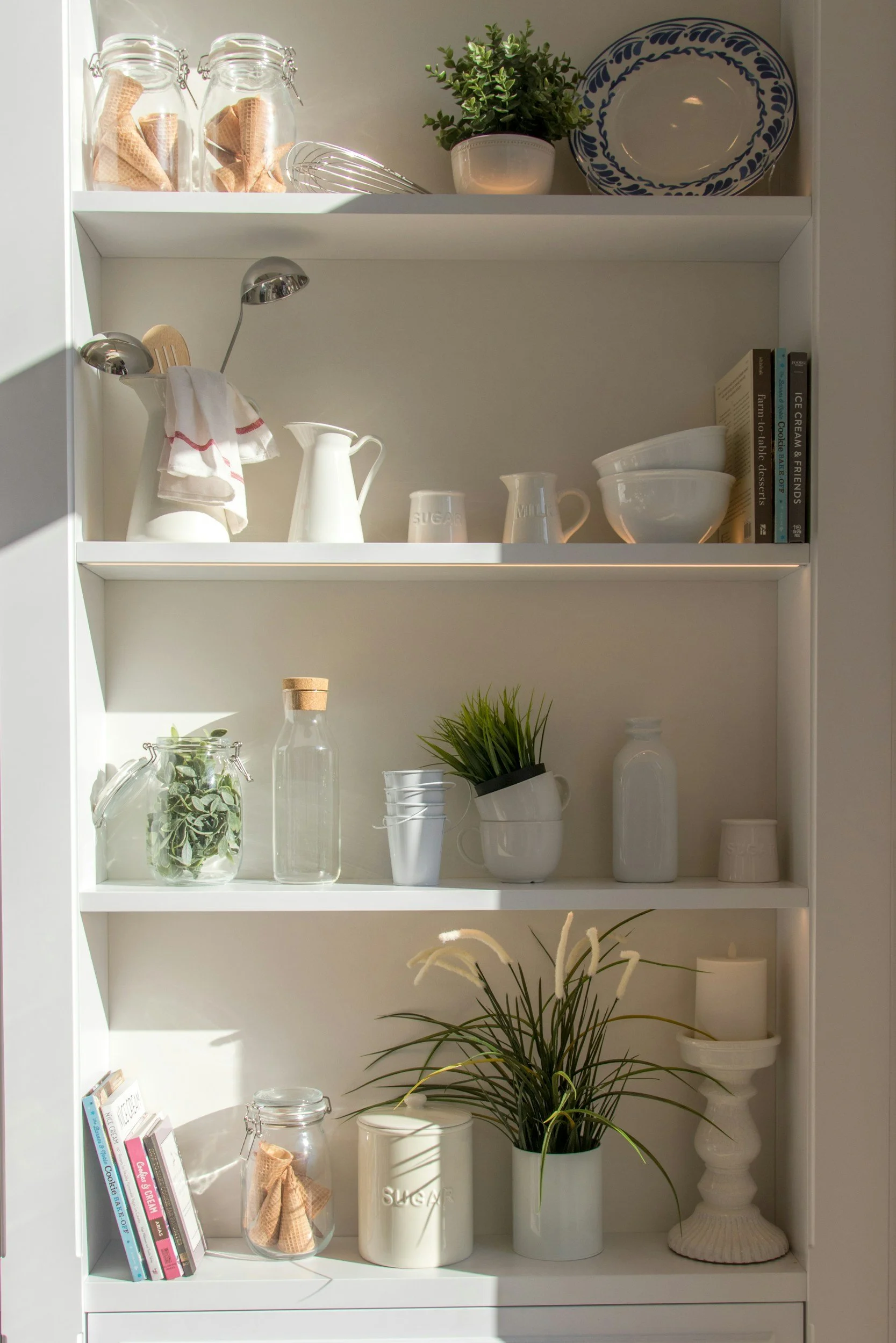 Open shelving with glass jars, white ceramics and a trailing plant in a softly lit kitchen.
